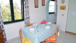 Un comedor con una mesa dispuesta para cuatro, sillas con cojines estampados, una ventana con cortinas y cuadros en la pared.