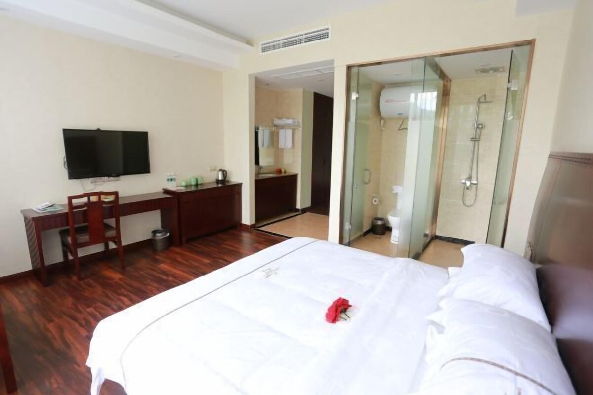 Habitación de hotel con cama, escritorio, silla, televisor y zona de ducha.