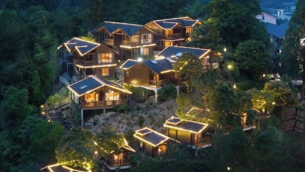 Un conjunto de cabañas de madera con varios niveles y balcones interconectados, rodeado de un bosque denso.