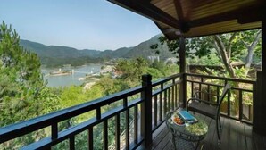 Terraza de madera con mesa y sillas, con vista a un río y montañas.