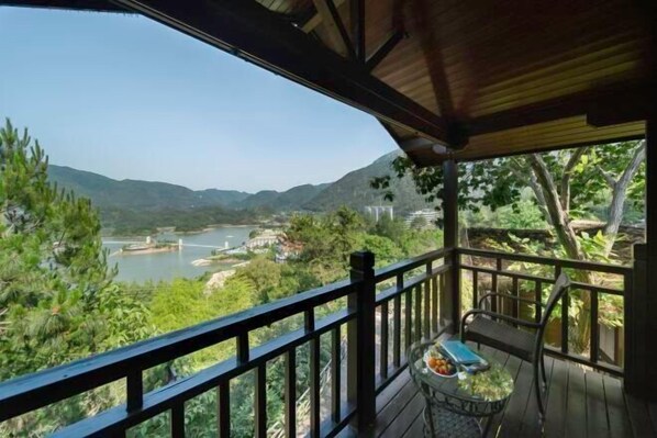 Terraza de madera con mesa y sillas, con vista a un río y montañas.
