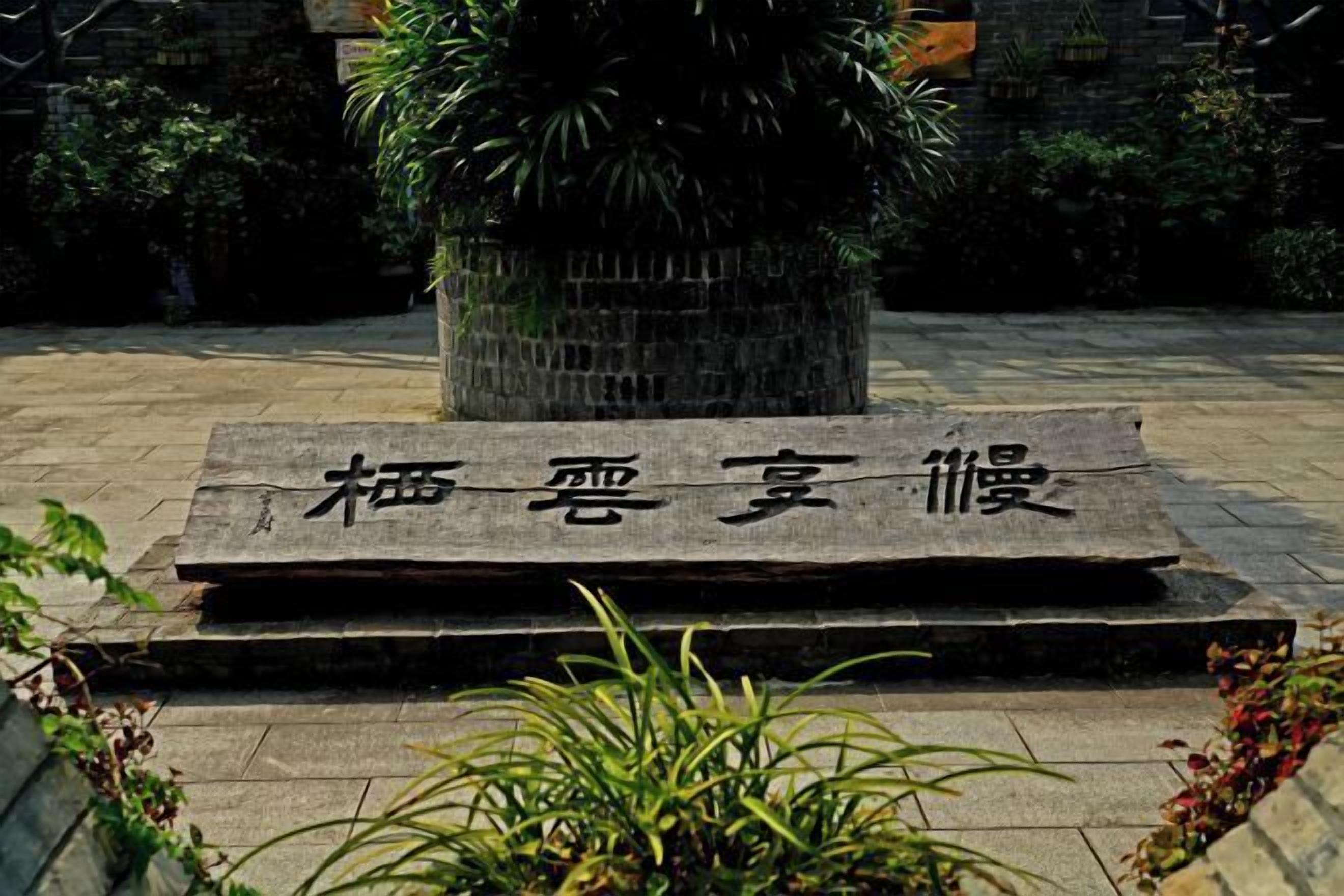 A stone plaque with Chinese characters in a courtyard with a potted plant and stone walls.