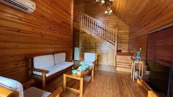 L'intérieur d'un chalet en bois, avec un canapé, une table, un téléviseur et un escalier.