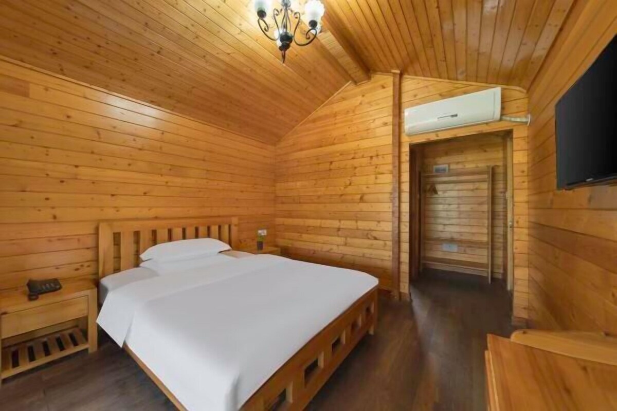 Habitación de cabaña de madera con una cama, una mesita de noche, una lámpara en el techo y una puerta que da a otra habitación.