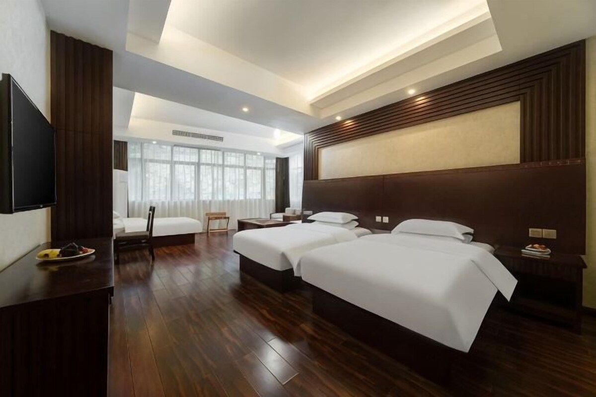 A hotel room with two beds, a flat-screen TV, a desk, and a large window.