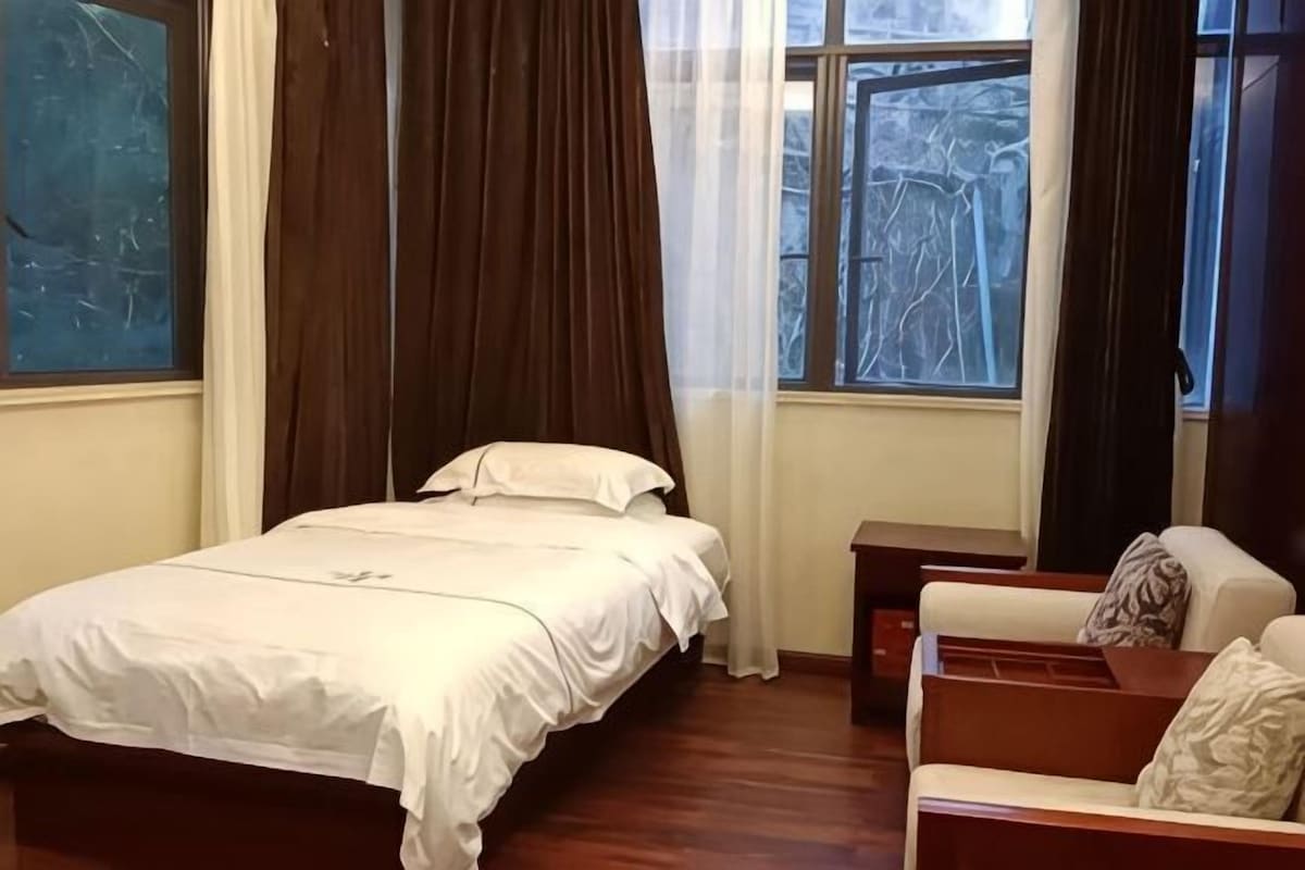 A room with a bed, a wooden nightstand, a chair, and a window with curtains.