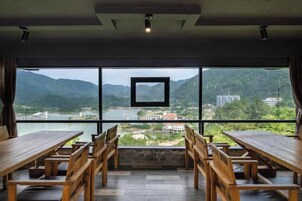 Uma área de refeições com mesas e cadeiras, grandes janelas com vista para montanhas e um rio.