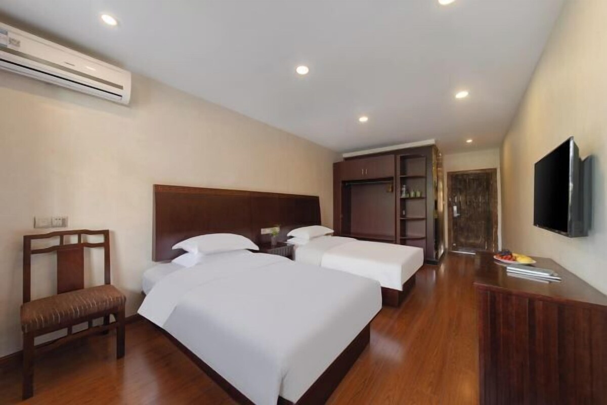 Habitación de hotel con dos camas, un banco de madera, un escritorio, un televisor y un armario.