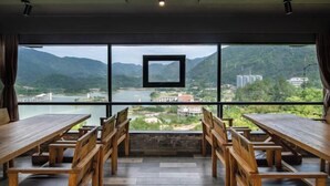 Comedor con mesas y bancos de madera, ventanas amplias con vistas a montañas y un río.