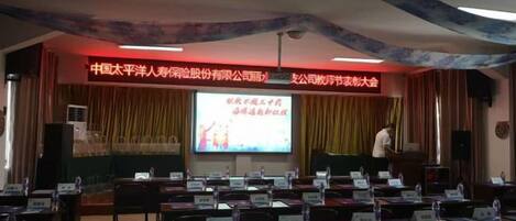 A conference room with a stage, a presentation screen, and rows of tables with nameplates.