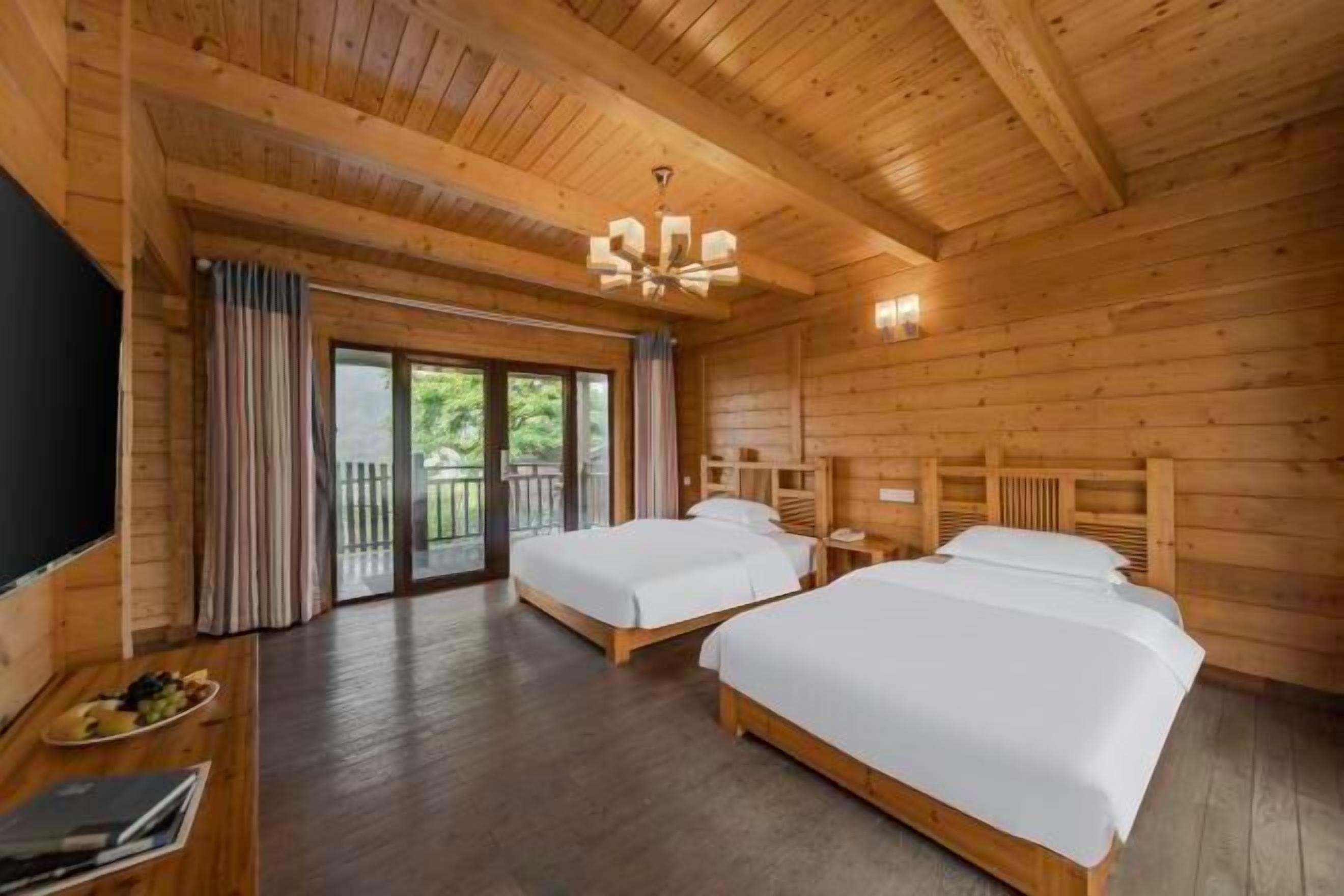 A wooden cabin-style room with two beds, a TV, and a balcony.