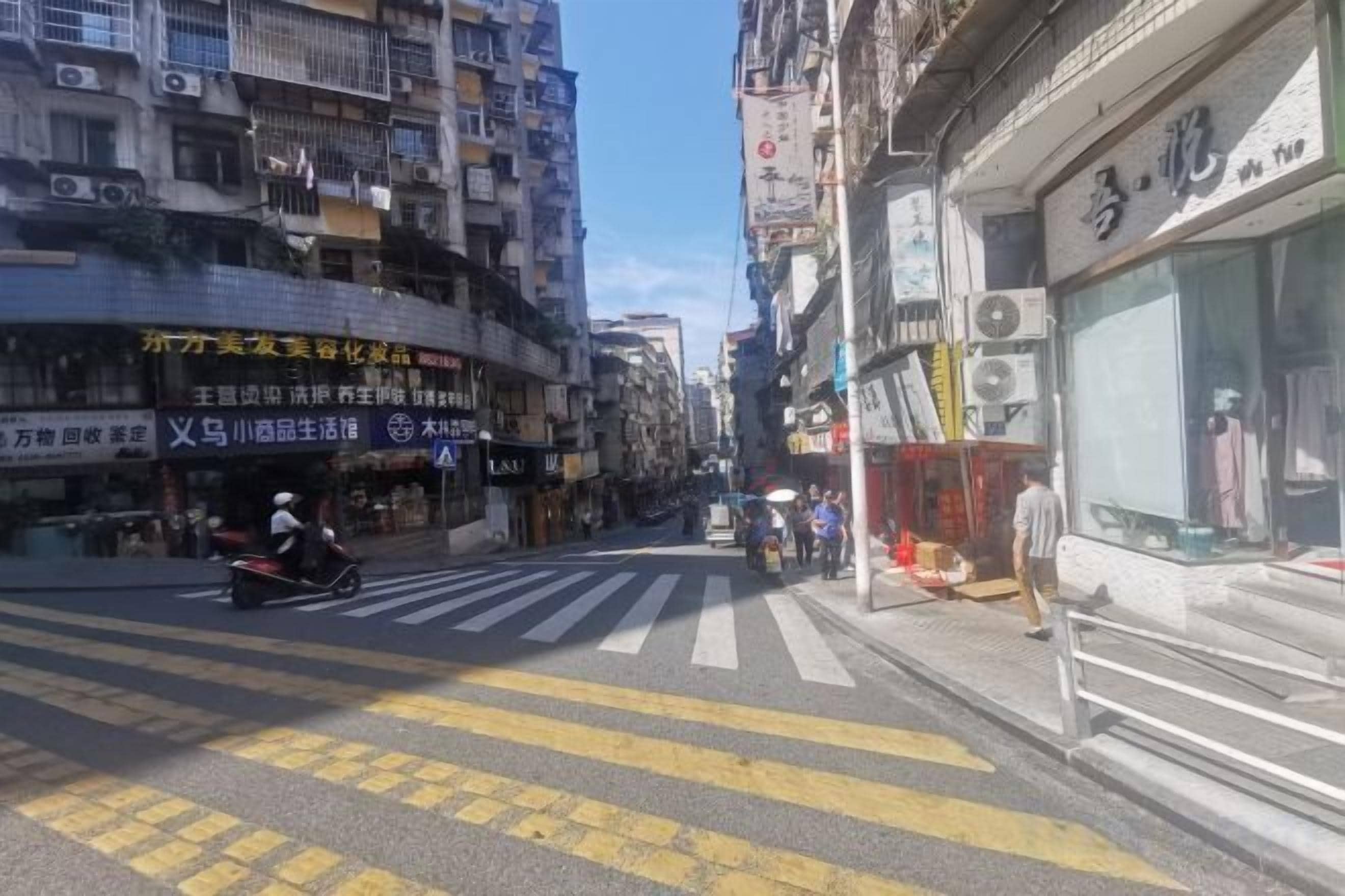 Vista de calle con edificios, un paso de cebra y un comercio con un letrero.