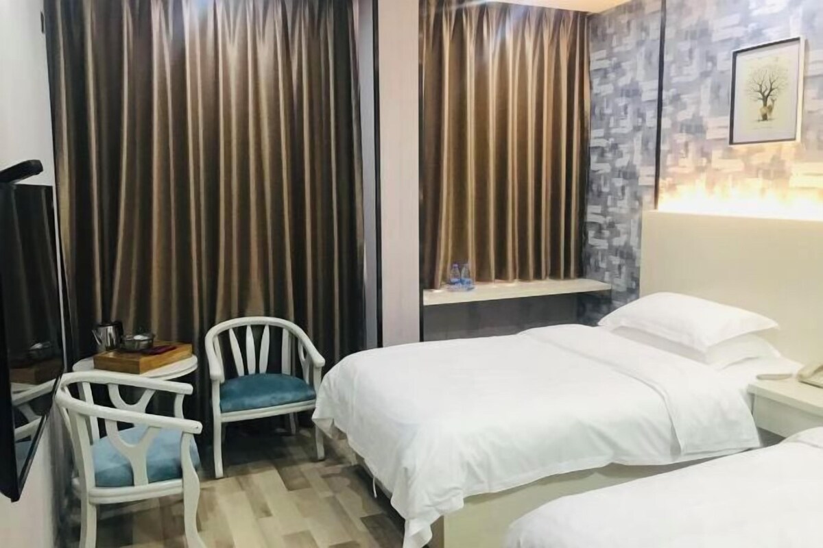 Habitación de hotel con dos camas, una silla, una mesita con una botella y un espejo.