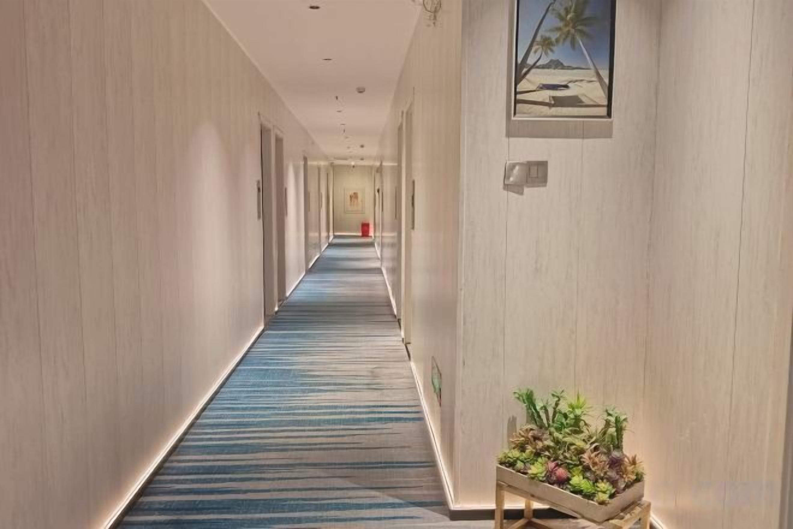 Ein Hotelgang mit blauem Teppich, Wandverkleidungen aus Holz und einer Pflanzenausstellung.