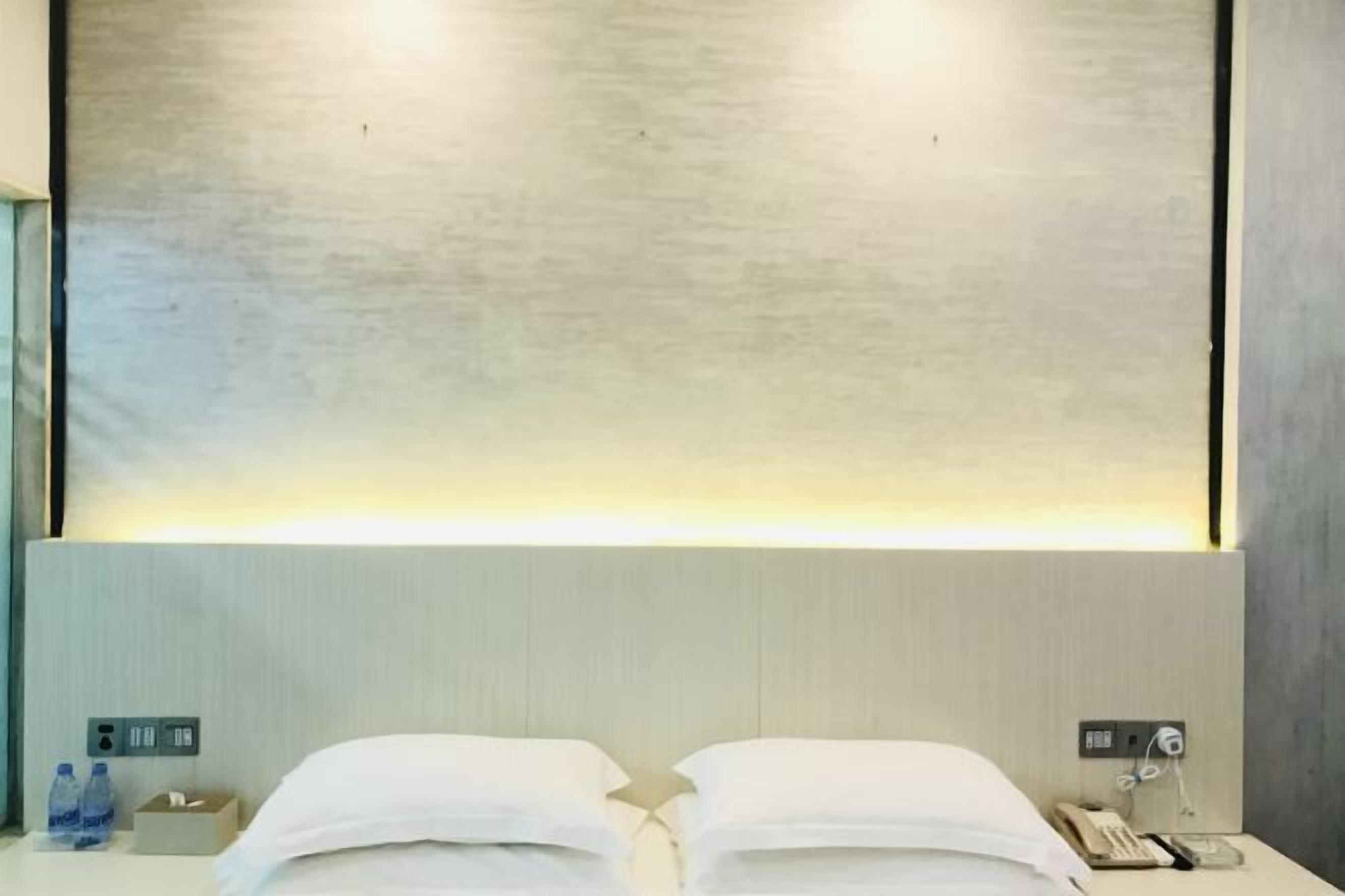 Une chambre d’hôtel avec deux lits, une table de chevet avec un téléphone et une bouteille d’eau, et un luminaire fixé au mur.