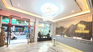 Een moderne hotel lobby met een receptiebalie, decoratieve planten en uitzicht op de straat.