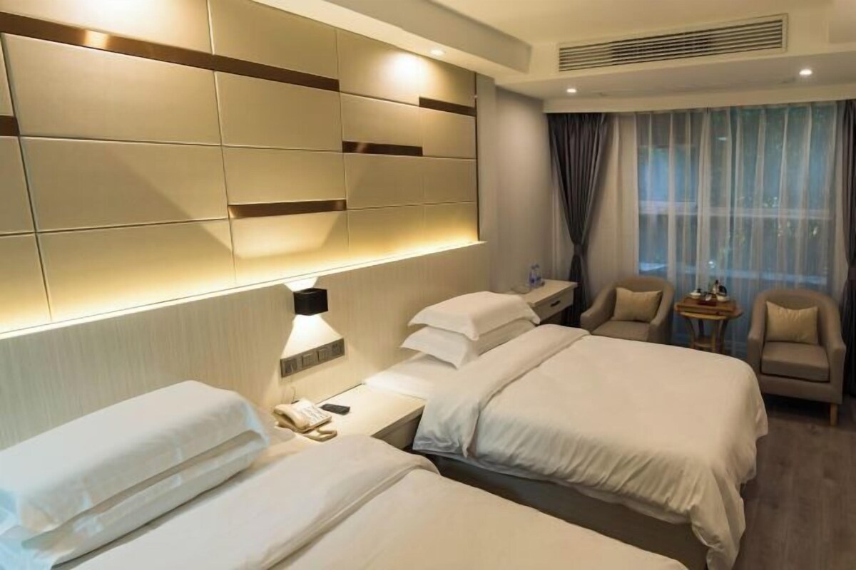 Habitación de hotel con dos camas, un escritorio con lámpara, una silla y vistas al exterior a través de una ventana.