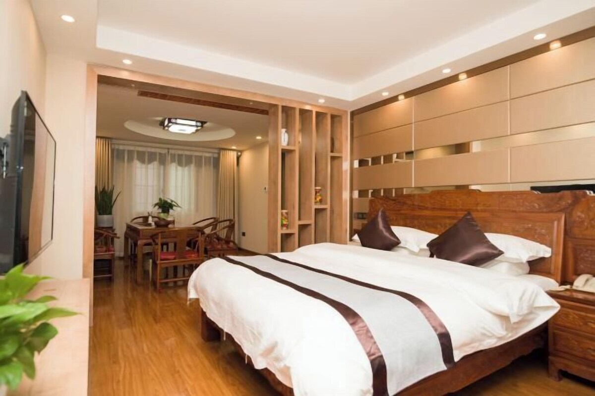Una habitación de hotel moderna con una cama grande, cabecera de madera, estanterías empotradas y una zona de comedor con sillas y mesa.