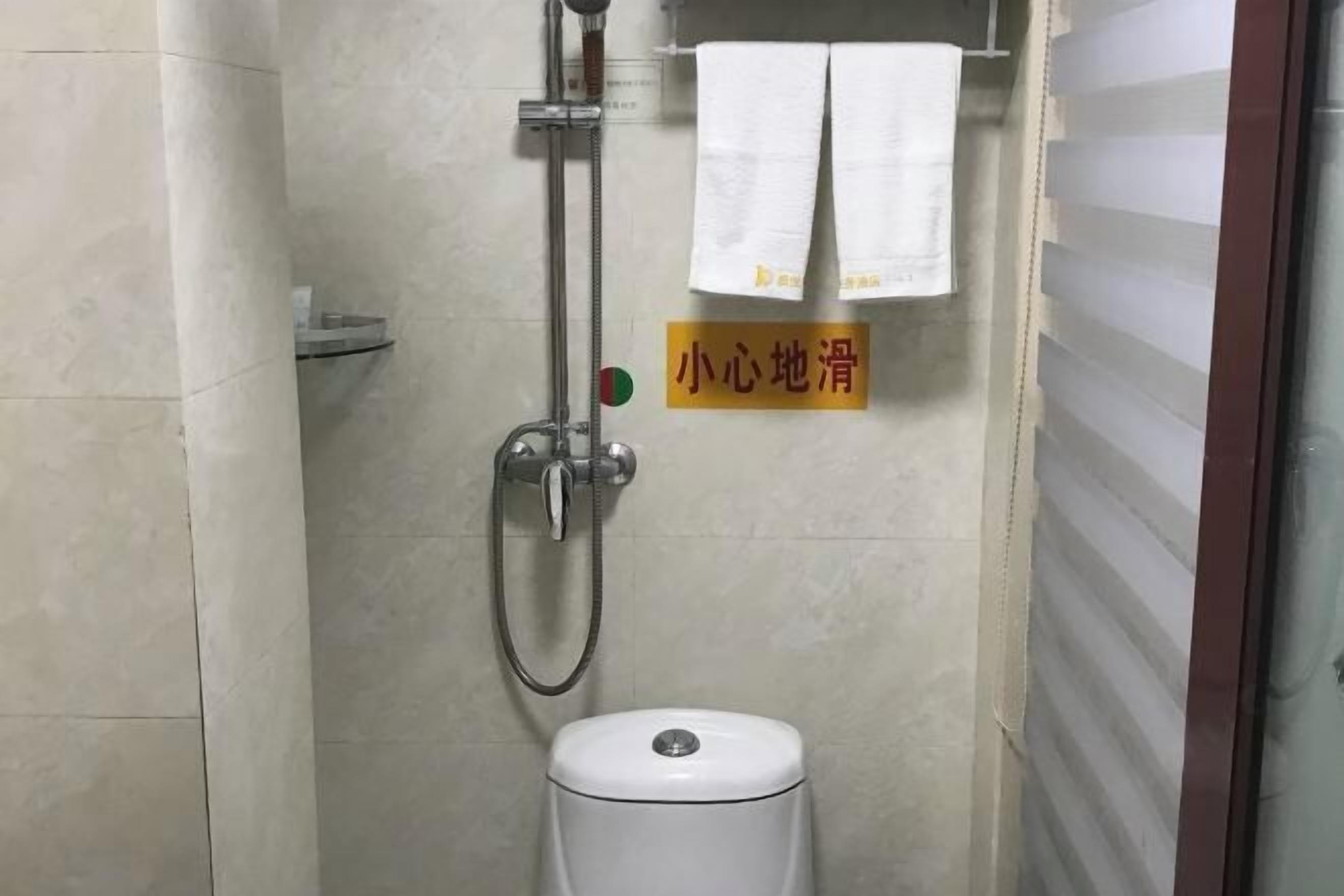 A small bathroom with a shower, toilet, and a sign on the wall.