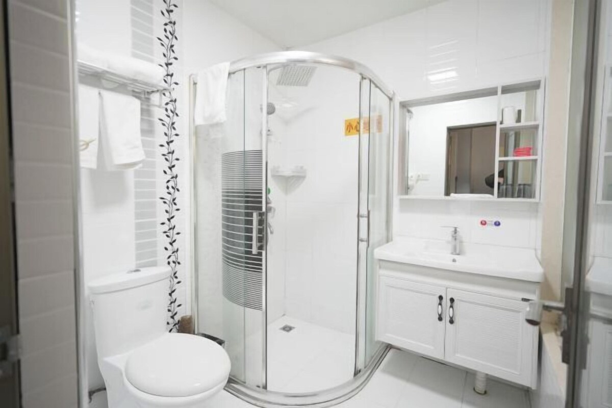 Un baño moderno con ducha envuelta en vidrio, inodoro blanco y tocador con espejo y lavabo.