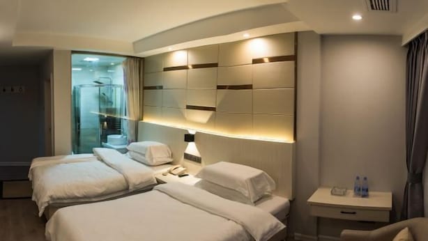 Een hotelkamer met twee bedden, een nachtkastje met een lamp, een klein bureau met een stoel en uitzicht op een badkamer.