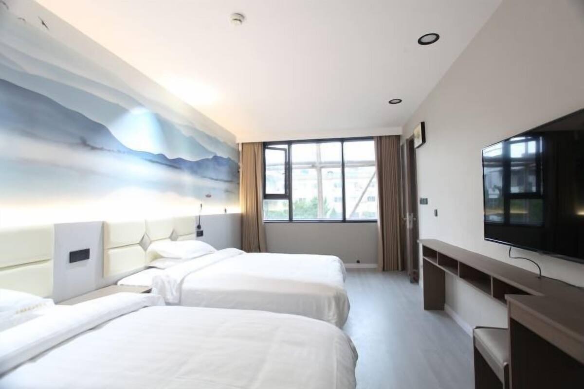 A hotel room with two beds, a large window, a flat-screen TV, and a painting on the wall.