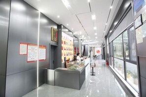 Un hall d’hôtel moderne avec un comptoir d’accueil, des affiches d’information et une exposition d’objets aux couleurs vives.