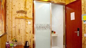 A wooden-paneled room with a sliding glass door leading to a shower area. There is a small shelf with toiletries and a vase of flowers. - Wuzhen Zhonglitunta Chinese Inn (Tongxiang)
