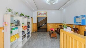 A reception area with a wooden reception desk, a staircase leading to an upper floor, and shelves with various items on the left. - Wuzhen Zhonglitunta Chinese Inn (Tongxiang)