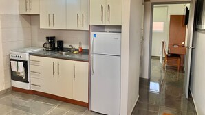 A compact kitchen with white cabinets, a built-in oven, a coffee maker, and a refrigerator.