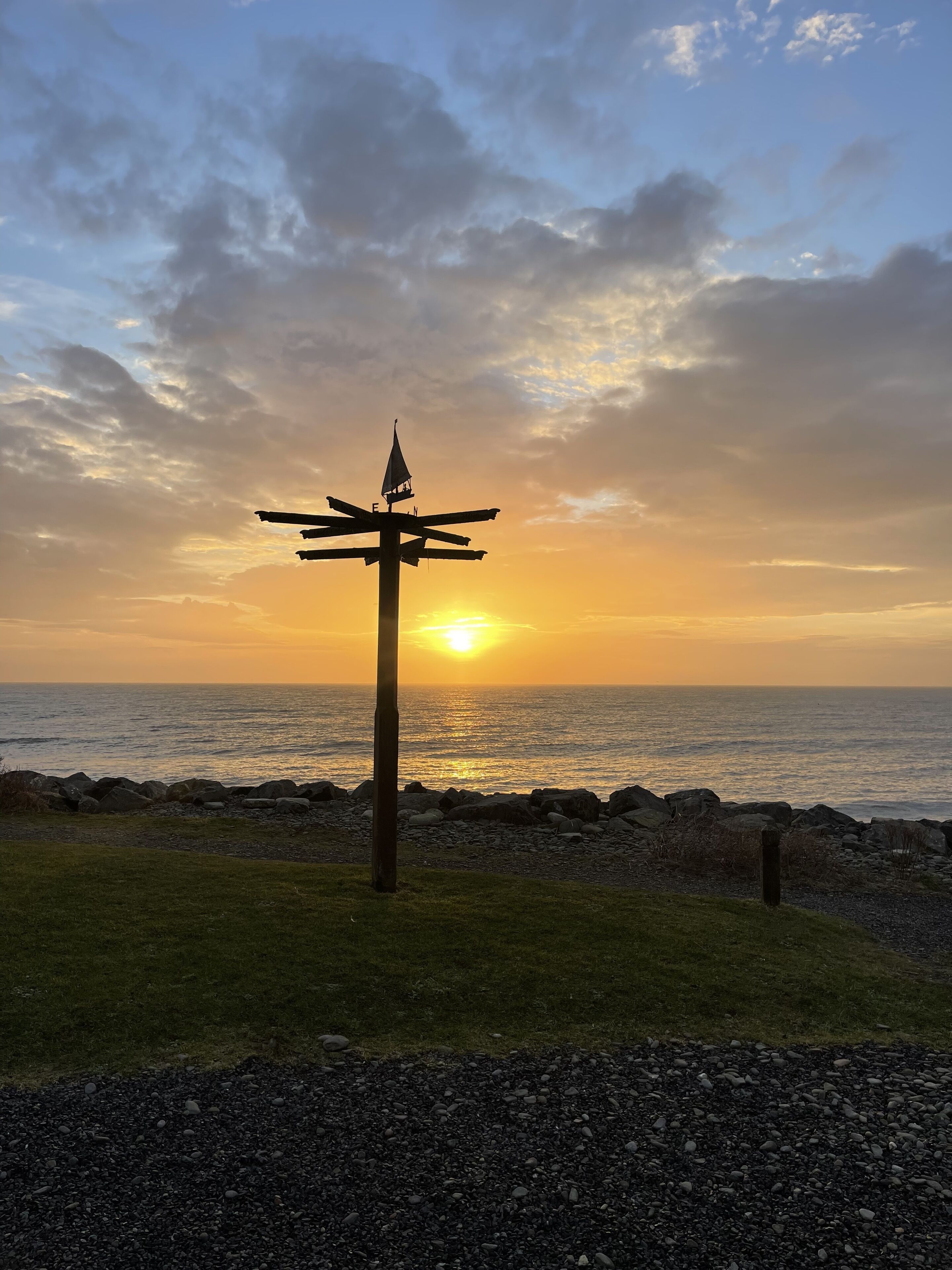 A sunset view with a directional signpost by the sea.