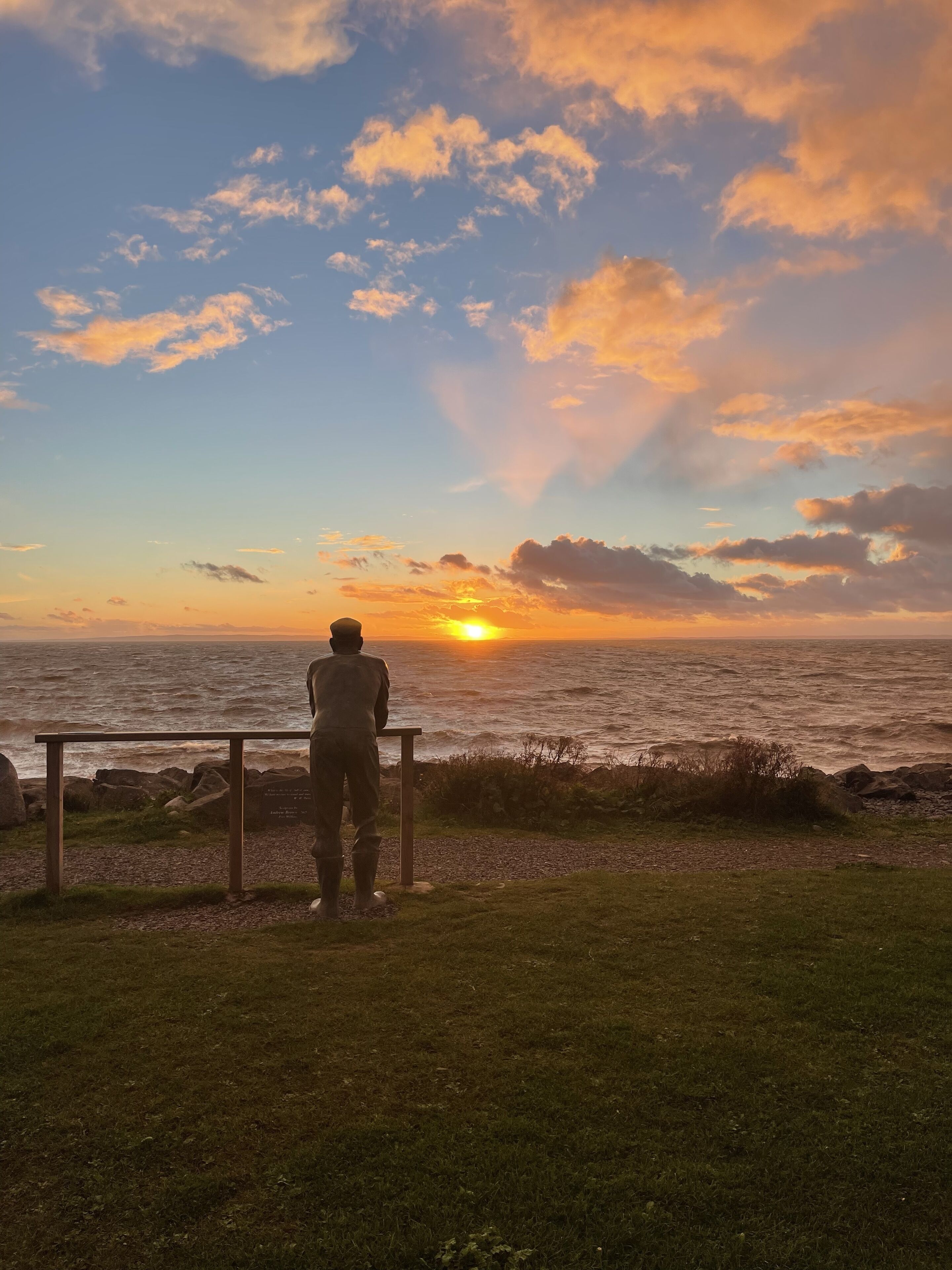 A person standing by a railing overlooking a sunset over the ocean.