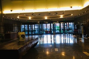 Eine Lobby mit einer Rezeption, einer großen Vase und einem Glastür-Eingang.