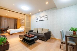 A modern hotel room with a bed, a sofa, a coffee table, and a dining area with a table and chairs. - Sunny International Apartment (Tianjin)