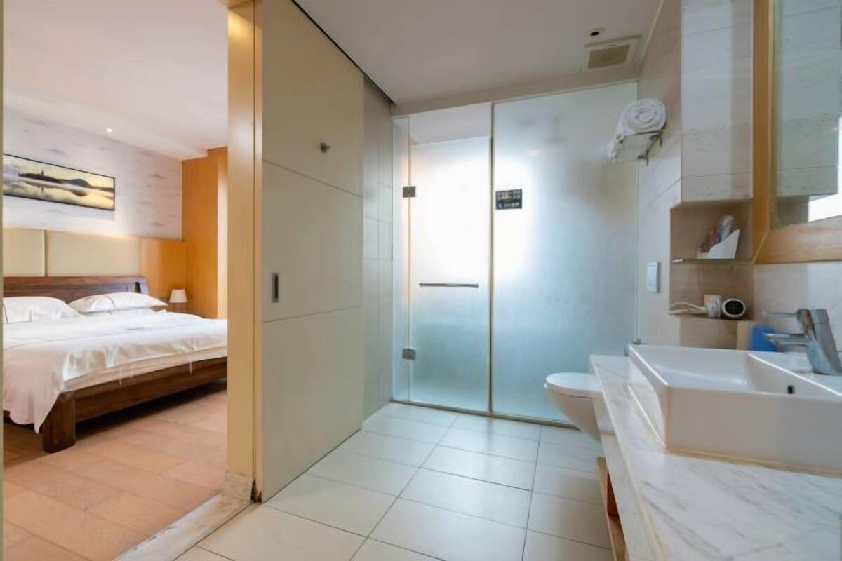 Une chambre d’hôtel moderne comprenant un lit, une salle de bain avec une douche à parois de verre et un lavabo en marbre.