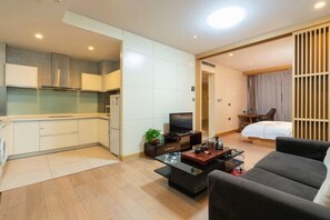 A compact hotel room with a kitchenette, a flat-screen TV, a sofa, and a bed. - Sunny International Apartment (Tianjin)