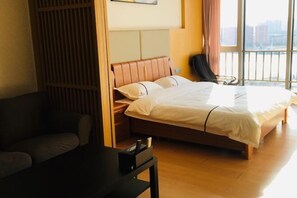 A hotel room with a bed, a desk, and a view of the city through large windows.
