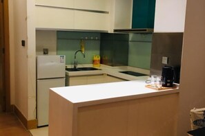 A compact kitchen with a white countertop, a sink, a stove, and a coffee maker.