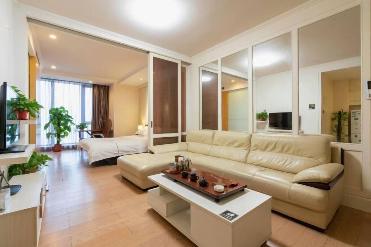 Un salon moderne avec un canapé, une table basse et un téléviseur. On aperçoit des plantes et une fenêtre à l’arrière-plan.
