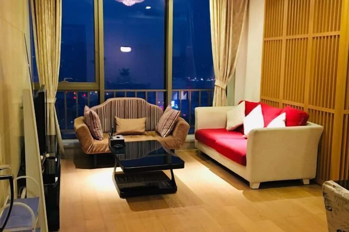 Un salon moderne avec un canapé et un fauteuil, une table basse en verre et de grandes fenêtres donnant sur la ville.