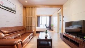 Une chambre d’hôtel moderne avec un canapé en cuir, un téléviseur à écran plat, une table basse en bois et un lit donnant sur l’extérieur.
