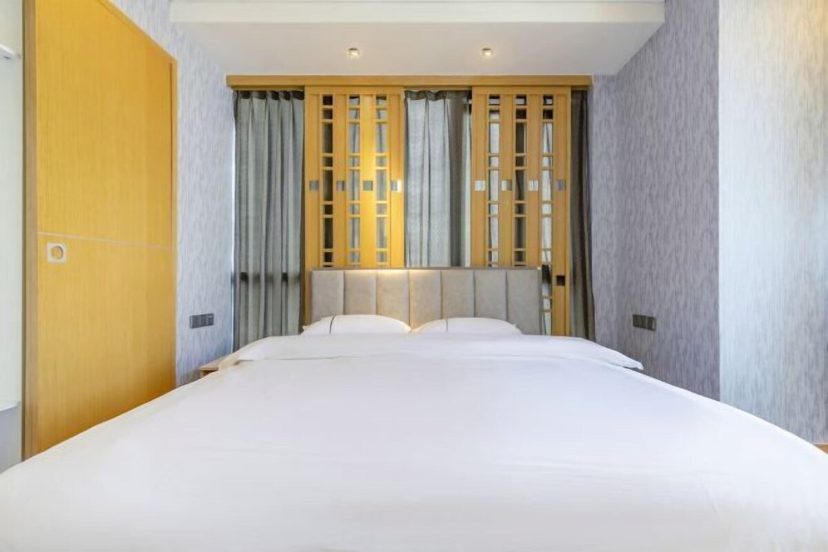 A hotel room with a large bed, a wooden headboard, and a curtain divider.