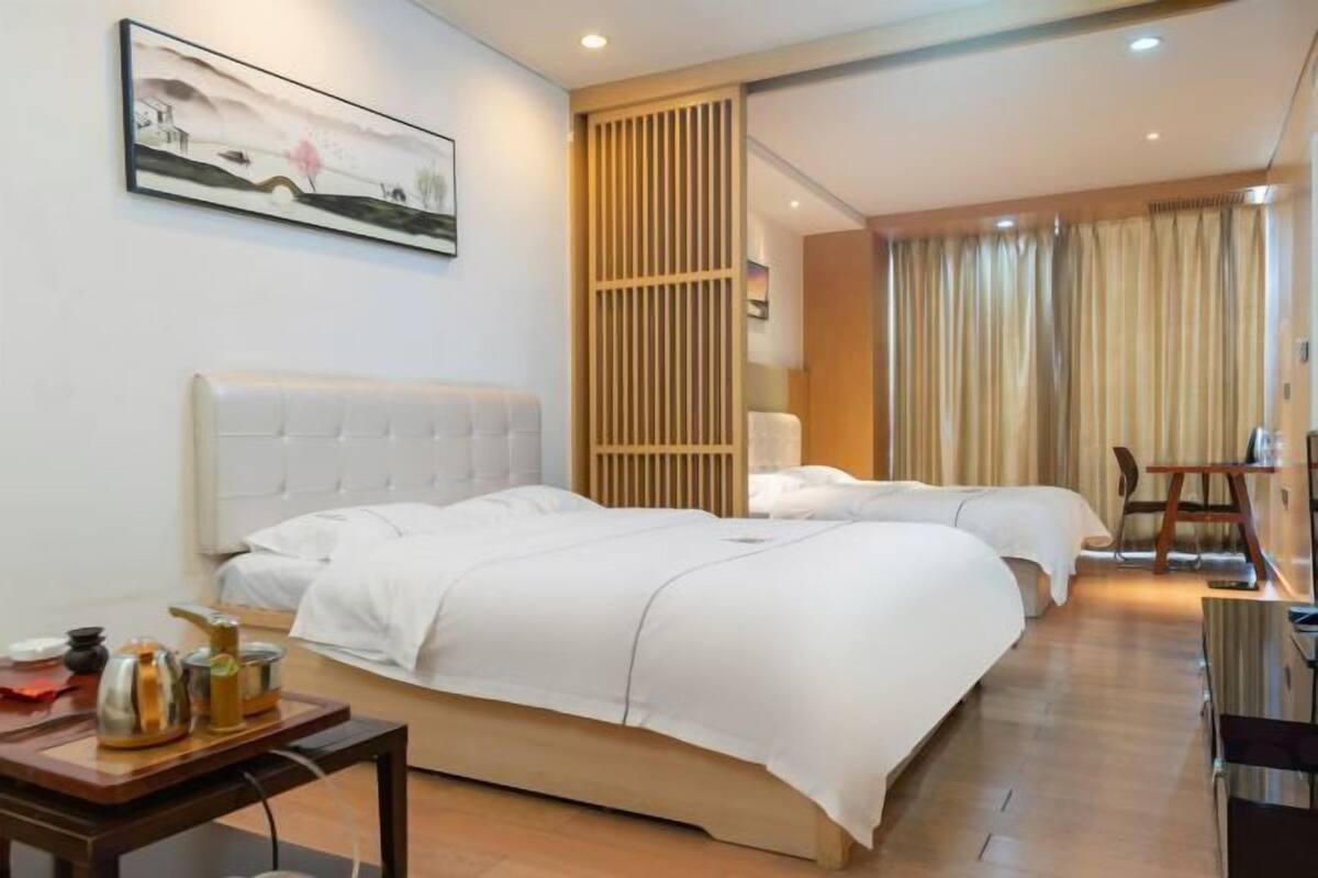 Une chambre d’hôtel avec deux lits, une cloison en bois, un bureau avec une chaise et un tableau au mur.