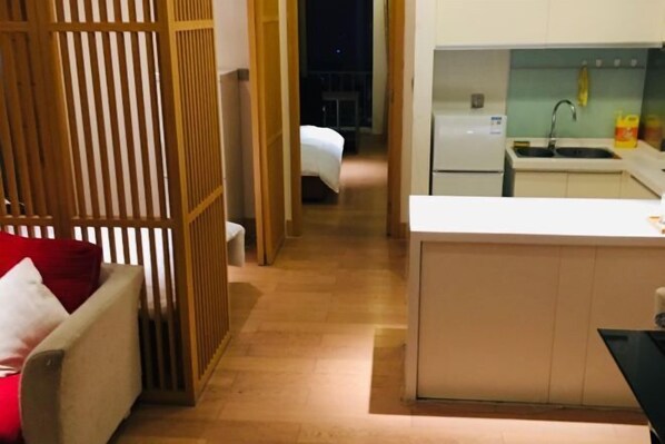 A hotel room with a wooden partition, a small kitchenette, a bed, and a red pillow.