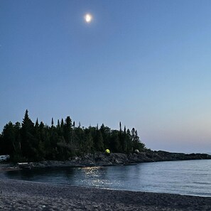 A beach with a forested area in the background and a clear sky.