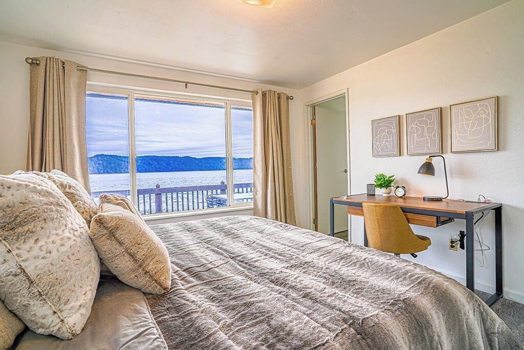Une chambre avec un grand lit, un bureau avec une chaise, une vue sur la mer et trois tableaux encadrés accrochés au mur.