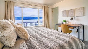 A bedroom with a large bed, a desk with a chair, a view of the sea, and three framed pictures on the wall. - Waterfront Retreat, Relaxation, Fun in Hood Canal (Hoodsport)