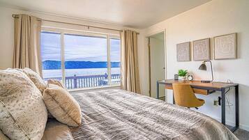 Une chambre avec un grand lit, un bureau avec une chaise, une vue sur la mer et trois tableaux encadrés accrochés au mur.