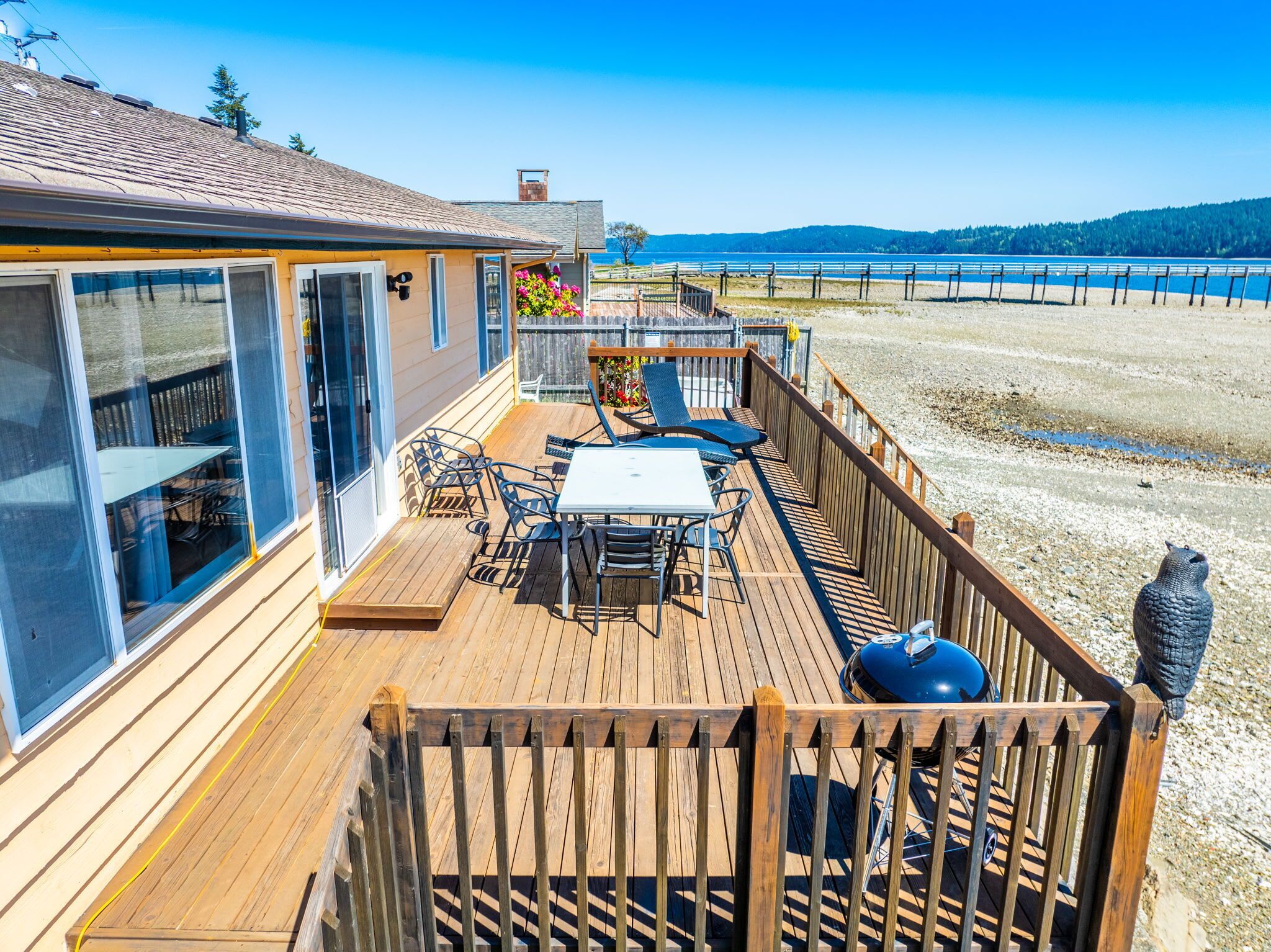 Une terrasse en bois avec une table et des chaises, donnant sur une plage et l’océan.