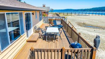 Une terrasse en bois avec une table et des chaises, donnant sur une plage et l’océan.